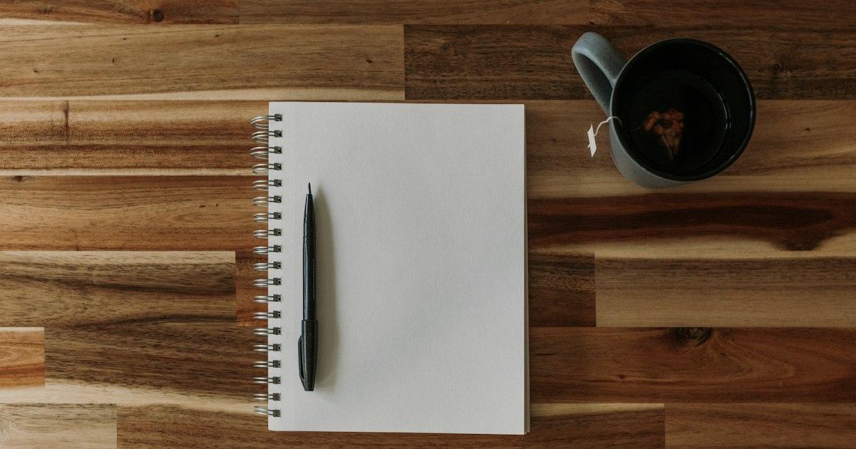 A notepad, pen and cup of coffee on a wooden table