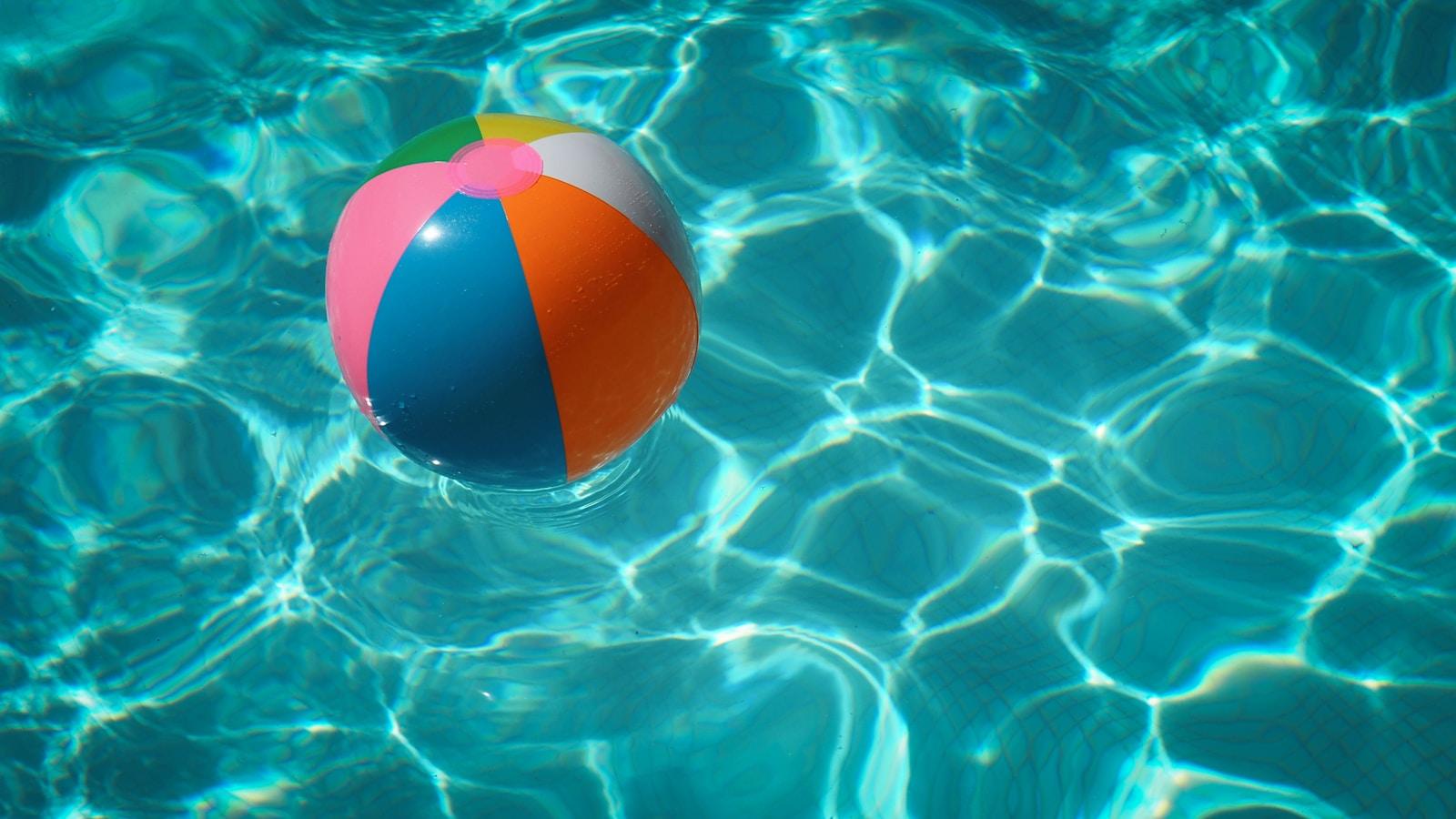 White and multicolored beach ball floating in a swimming pool