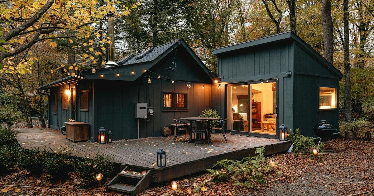 Small wooden vacation rental cabin with a lit deck in the woods at dusk